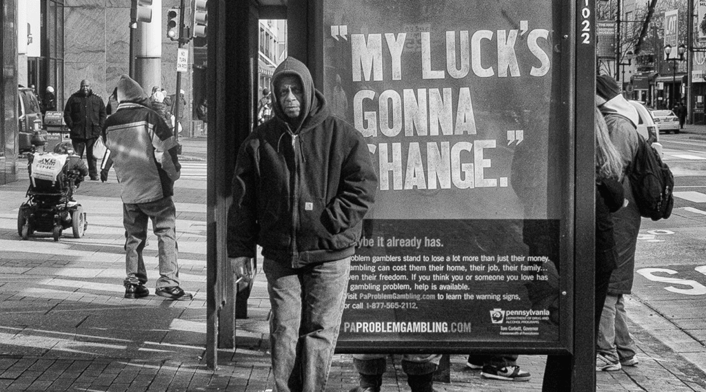 Man stands next to bus stop sign that reads "My luck's gonna change."
