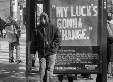Man stands next to bus stop sign that reads "My luck's gonna change."